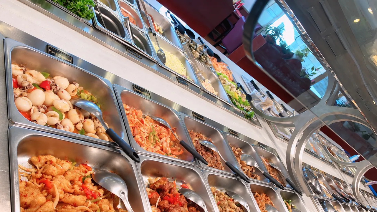 Rangée de bacs du buffet avec leurs étiquettes, poisson au piment au premier plan.