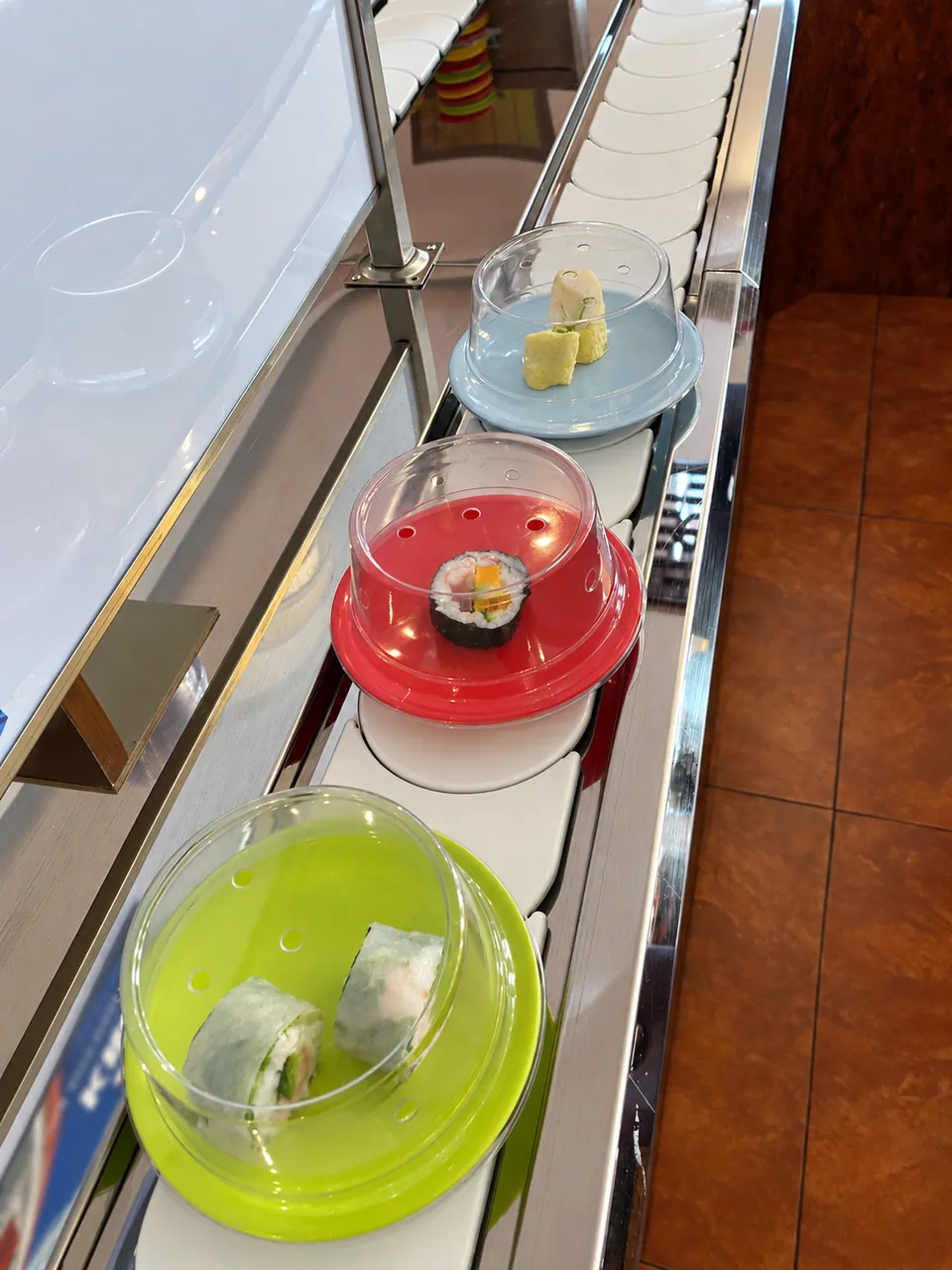 Trois petites assiettes sous cloche colorée (verte, rouge, bleue) sur le tapis roulant.