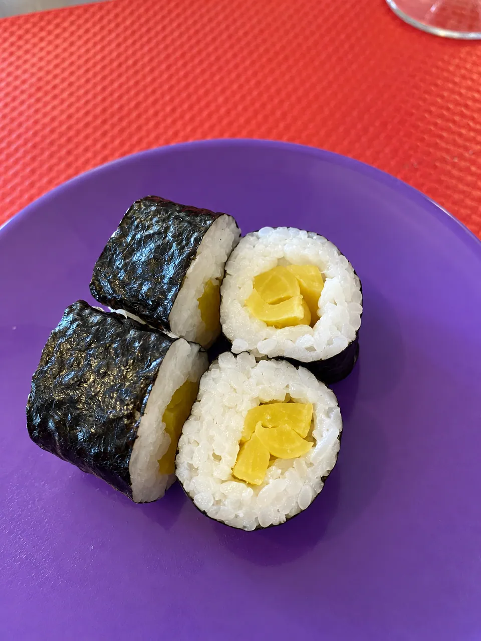 Quatre makis au radis mariné sur une assiette violette, set rouge.