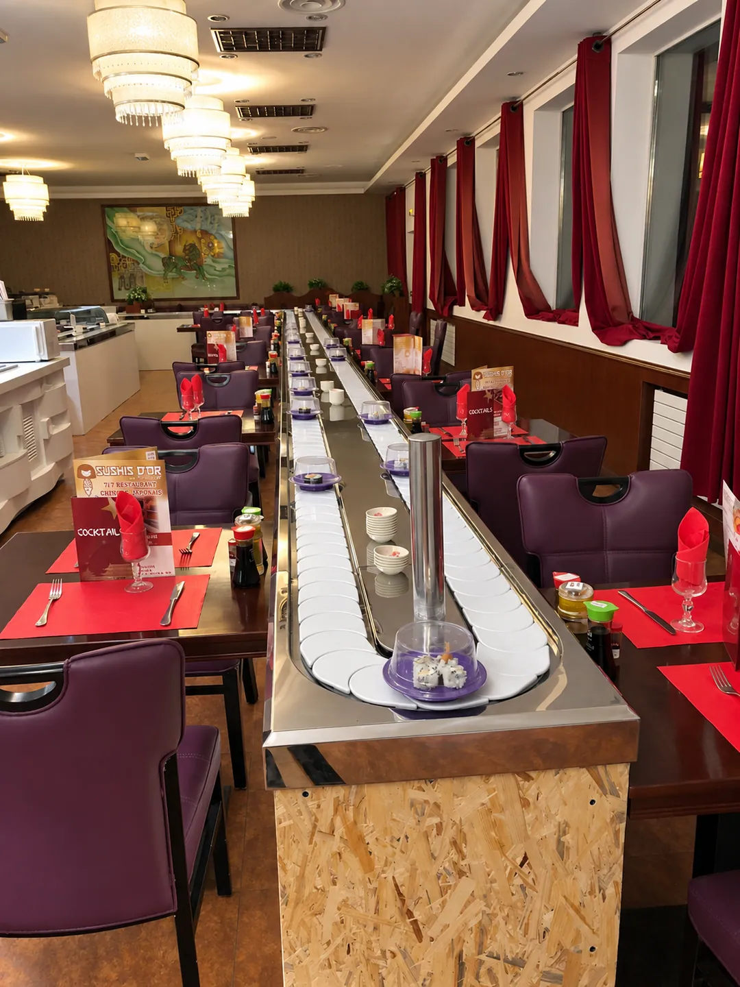 La salle du Sushi d'or : le tapis roulant à sushis traverse la salle entre les tables aux sets rouges.