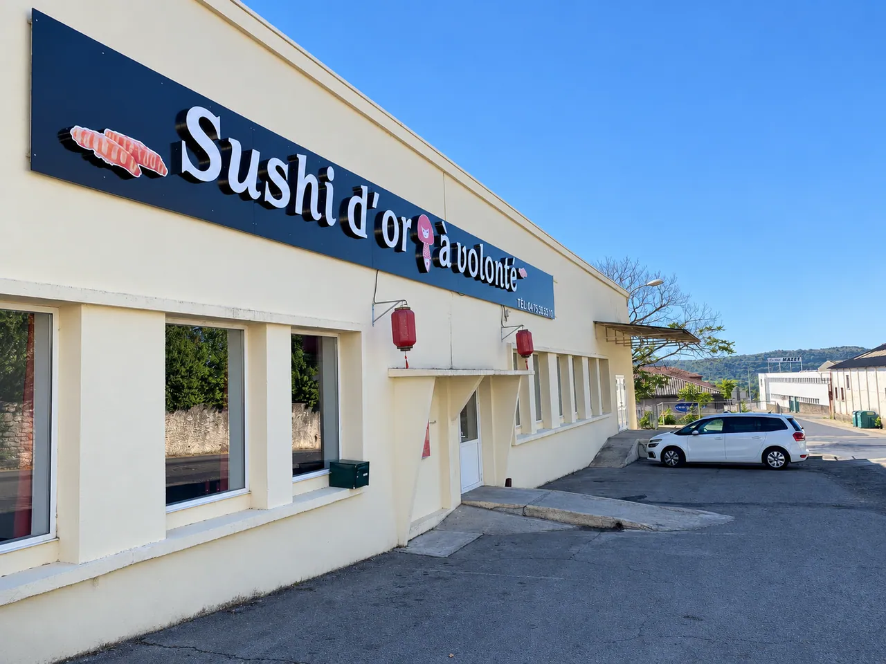 La façade du Sushi d'or à volonté : enseigne bleue, lanternes rouges et parking devant l'entrée.
